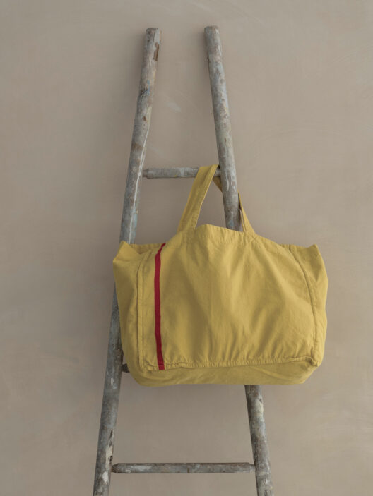 Yellow bag on rustic ladder against beige background.