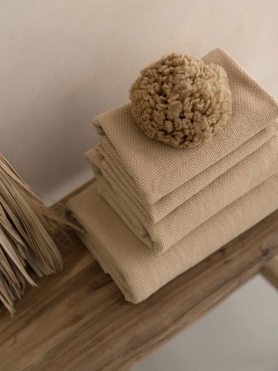 Serviettes beiges avec éponge sur banc en bois.