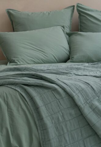 Lit avec draps verts et coussins assortis.