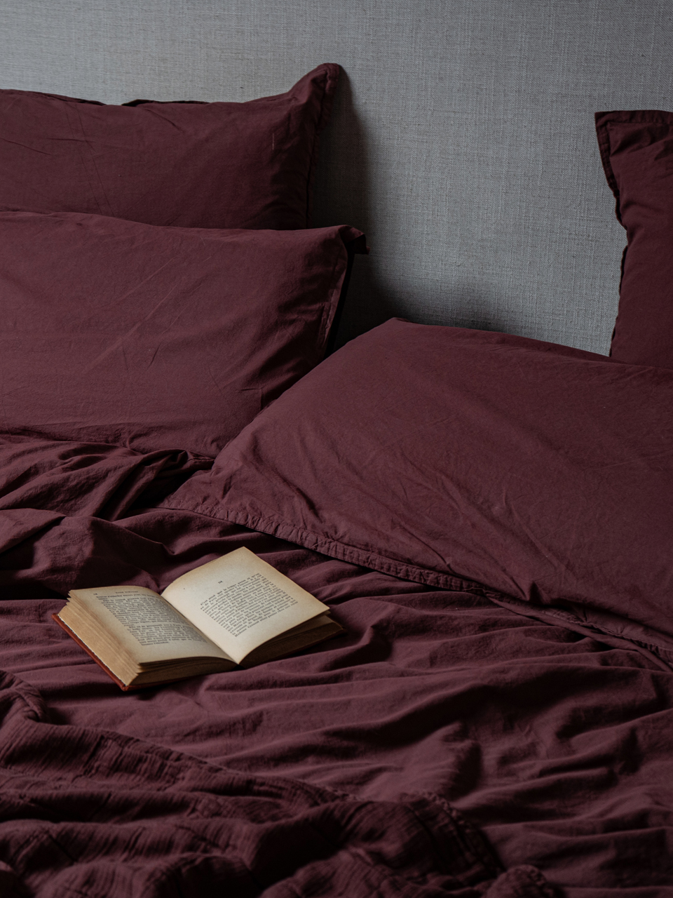 Lit avec couverture bordeaux et livre ouvert.