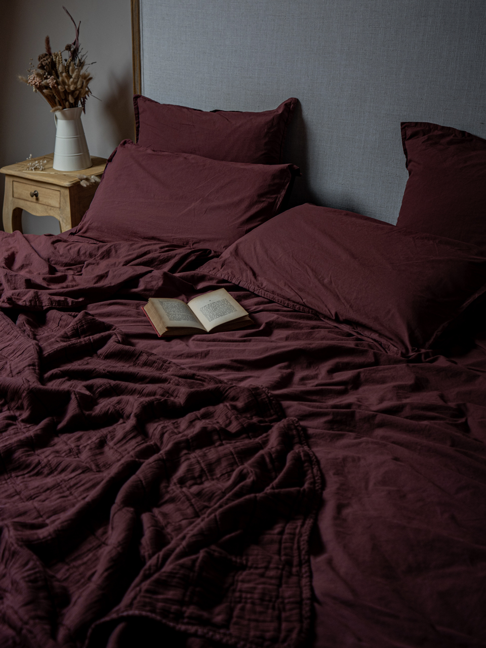 Lit avec couverture bordeaux et livre ouvert.