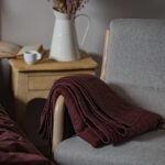 Plaid rouge sur fauteuil, vase et livre sur table.