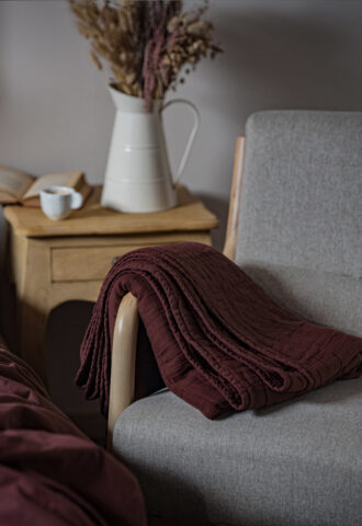 Plaid rouge sur fauteuil, vase et livre sur table.
