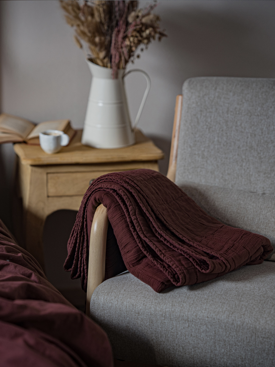 Plaid rouge sur fauteuil, vase et livre sur table.
