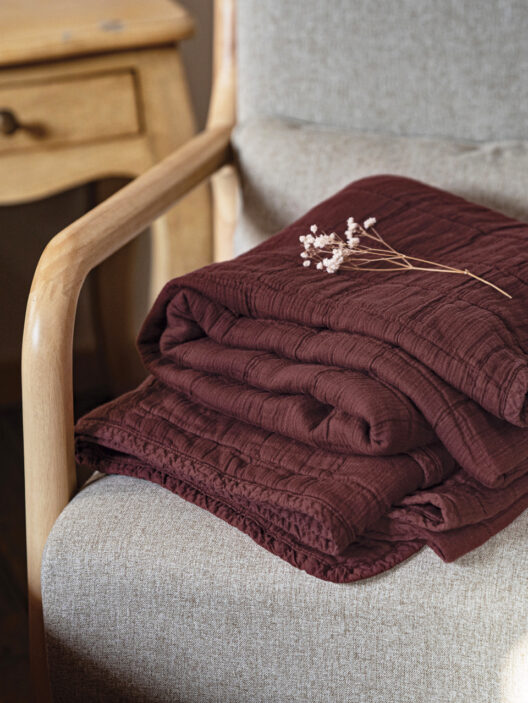 Plaid bordeaux plié sur fauteuil beige.