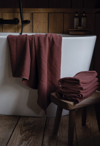 Serviettes bordeaux sur baignoire blanche et tabouret.