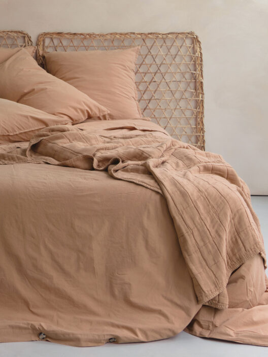 Lit avec draps beige et tête en rotin